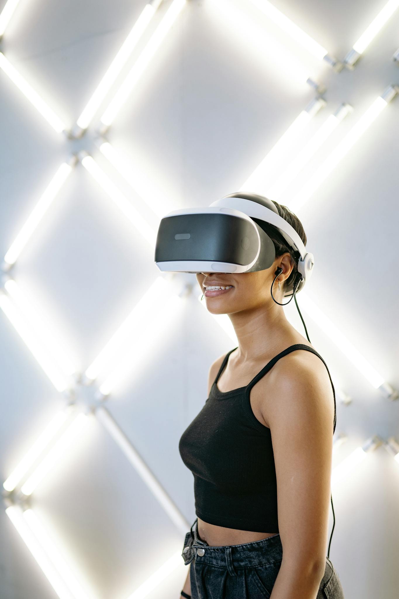 Young woman in a black tank top enjoying a virtual reality game with VR goggles in a studio.